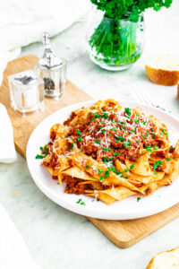 Overhead view of a round white plate piled high with a swirl of vegan bolognese on wide noodles