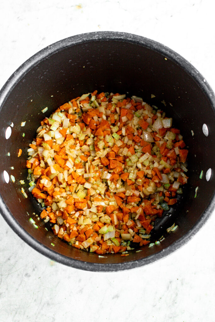 Overhead view of a large black soup pot filled with sauteed veggies