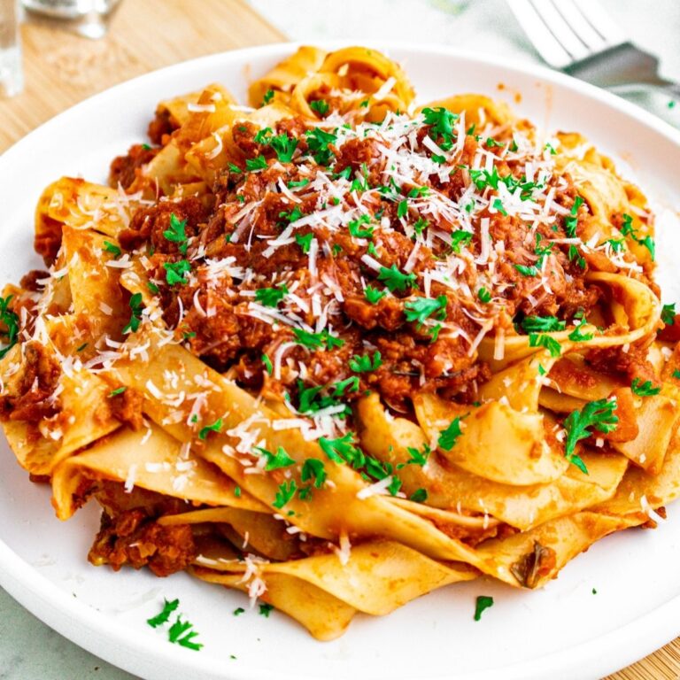 Overhead view of a round white plate topped with a large swirl of vegan bolognese noodles topped with fresh minced herbs