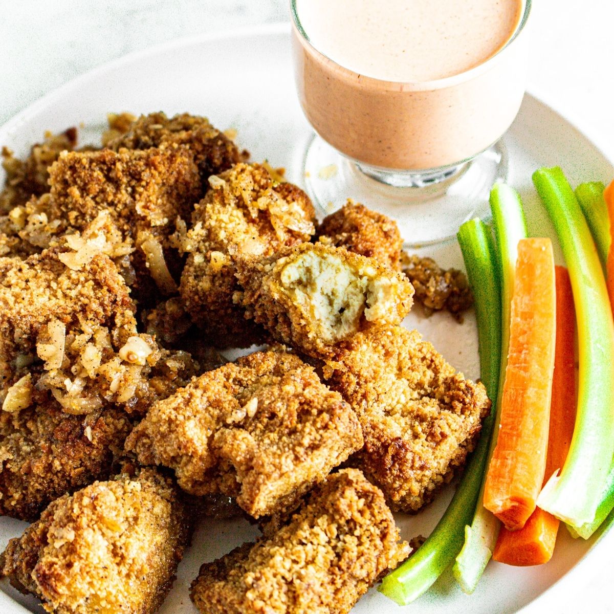 Overhead view of a round white plate with a pile of vegan garlic parmesan wings with a bite taken out of the top wing