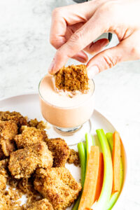 Overhead view of a hand dipping a vegan garlic parmesan wing into a clear glass jar of buffalo ranch