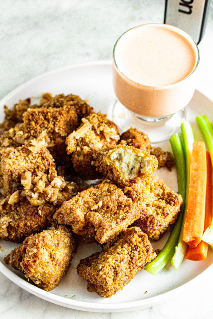 Overhead view of a round white plate with a pile of vegan garlic parmesan wings with a bite taken out of the top wing