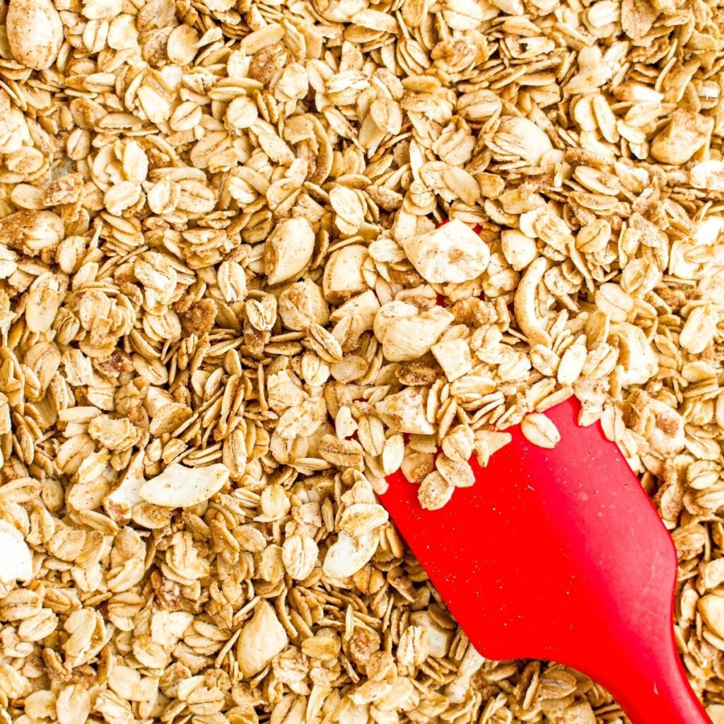 Close up overhead view of a red spatula pushing vegan granola