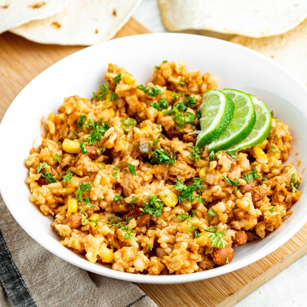 Overhead view of a round white bowl filled with crockpot vegan salsa chicken and rice topped with green herbs and lime slices