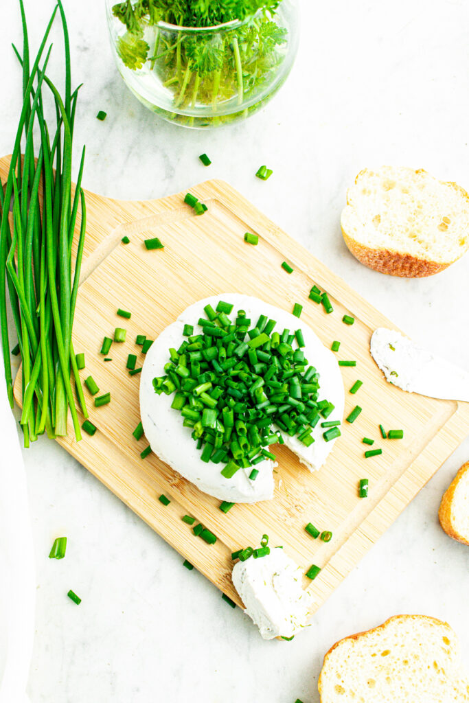 Overhead view of a round white vegan Boursin cheese wheel topped with chopped green onions surrounded by bread slices