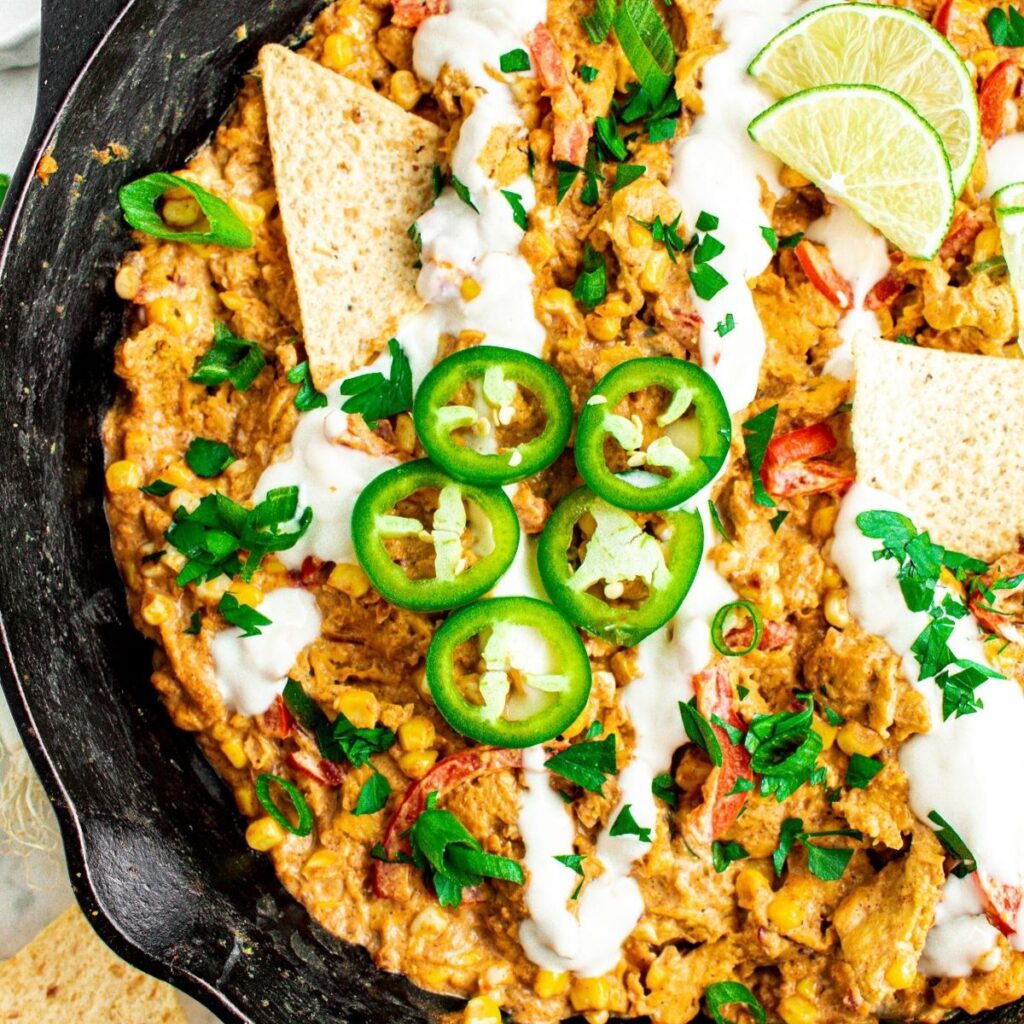 Overhead view of a cast iron skillet filled with creamy corn and soy curls topped with sliced jalapenos