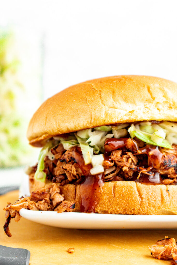 Close up head on view of a delightfully messy BBQ vegan pulled pork sandwich stuffed with jackfruit pulled pork on a toasted bun with green cabbage slaw